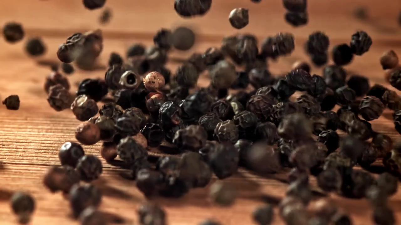 Svarte pepperkorn faller ned på en treoverflate i sakte film