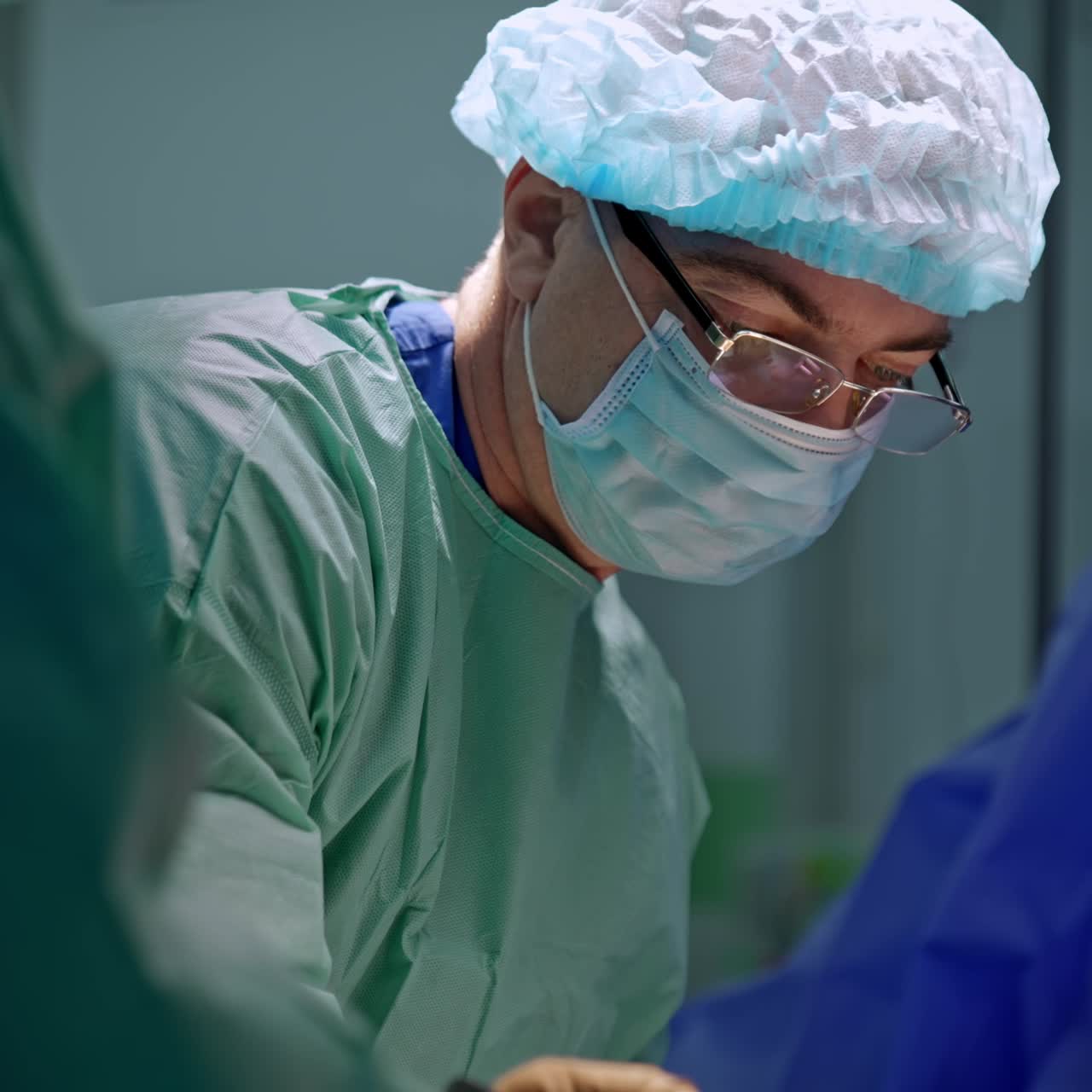 Orthopedic surgeon uses a metal mallet at operation. Focused doctor in eyeglasses, cap and mask close up portrait