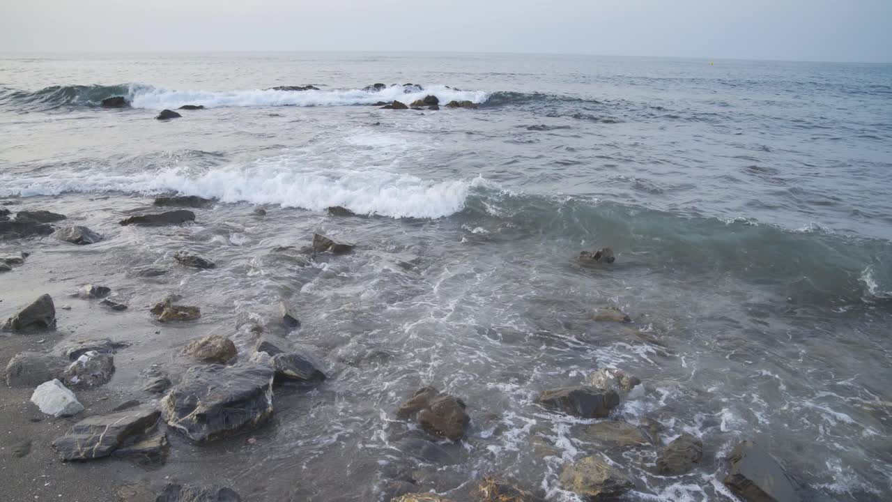 Light surf gently washes in as the cool morning light shines on the rocky beach near Cala de Mijas on the Costa Del Sol in Southern Spain