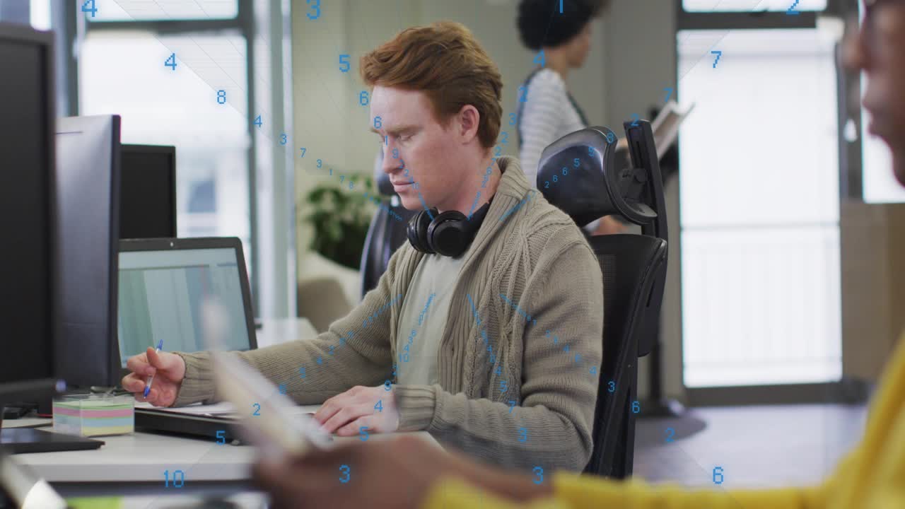 Male office worker typing and causing blue numeric overlay while scrolling and jotting notes