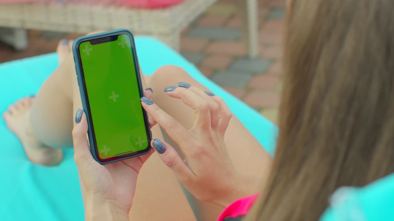 close up de la chica usando la pantalla verde del teléfono móvil mientras se relaja cerca de la piscina. manos sosteniendo la llave de cromo del teléfono inteligente, tocando la pantalla moderna del teléfono inteligente.