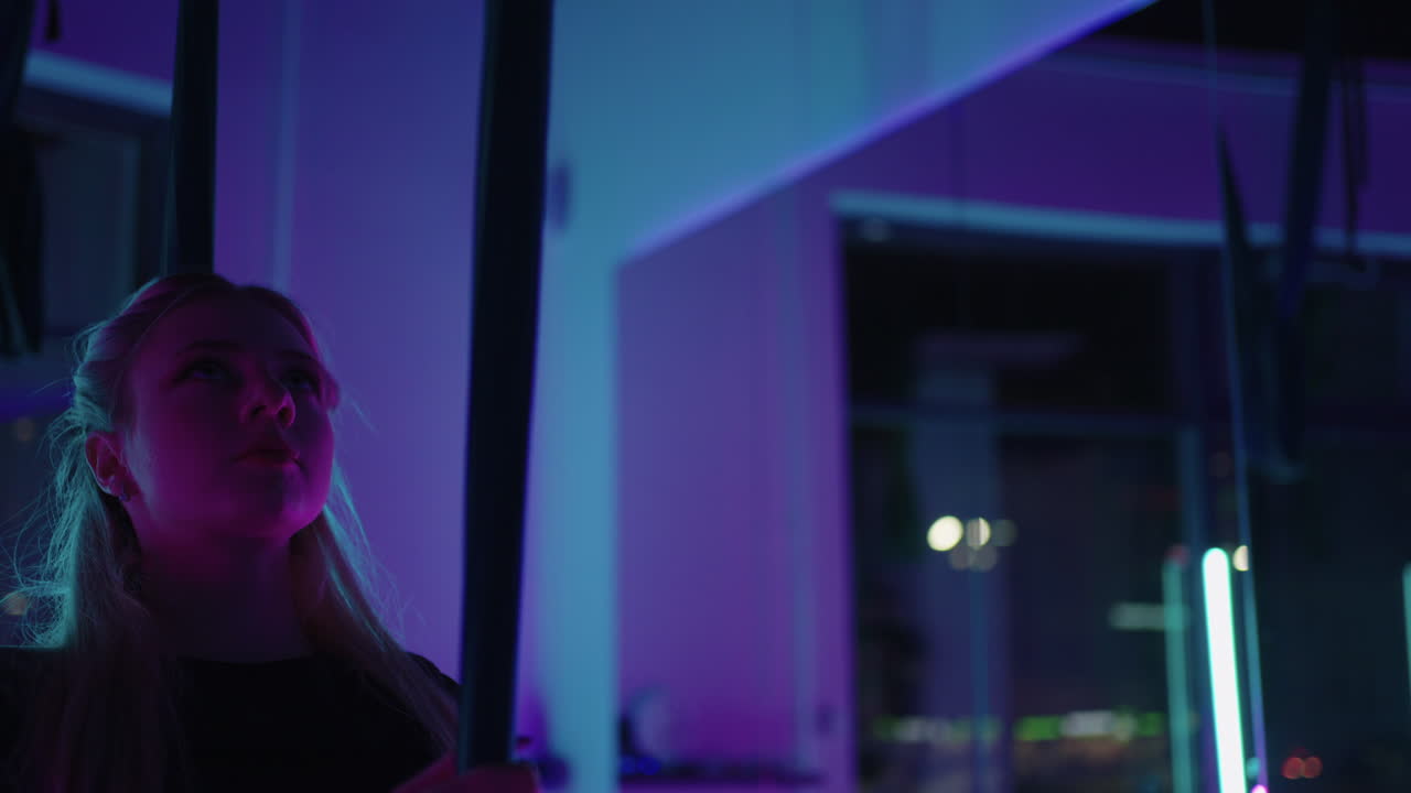 una mujer hace yoga deportivo en el aire en una hamaca a la luz del neón realizando ejercicios y movimientos graciosos de estiramiento y baile en cámara lenta.