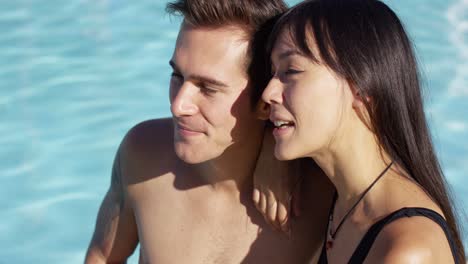 sunbathing couple sit beside swimming pool