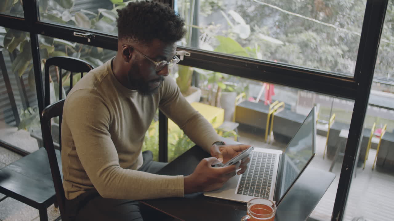 Man using smartphone and laptop in a cafe