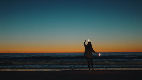 girl dancing with sparklers on beach at sunset celebrating new years eve woman having fun dance with sparkler fireworks enjoying independence day celebration by the sea