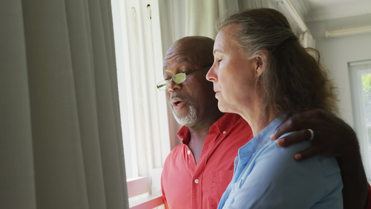 Happy senior diverse couple wearing shirts and embracing in living room