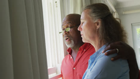 Happy-senior-diverse-couple-wearing-shirts-and-embracing-in-living-room