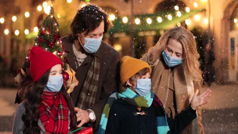 close-up view of caucasian happy family wearing facial masks walking down the street and holding christmas tree while it¬¥s snowing in christmas