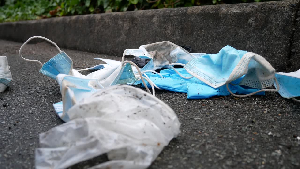 거리 보도에서 바람에 쓰레기를 불고 있는 더럽고 버려진 코로나 바이러스 마스크는 돌리 왼쪽을 닫습니다.