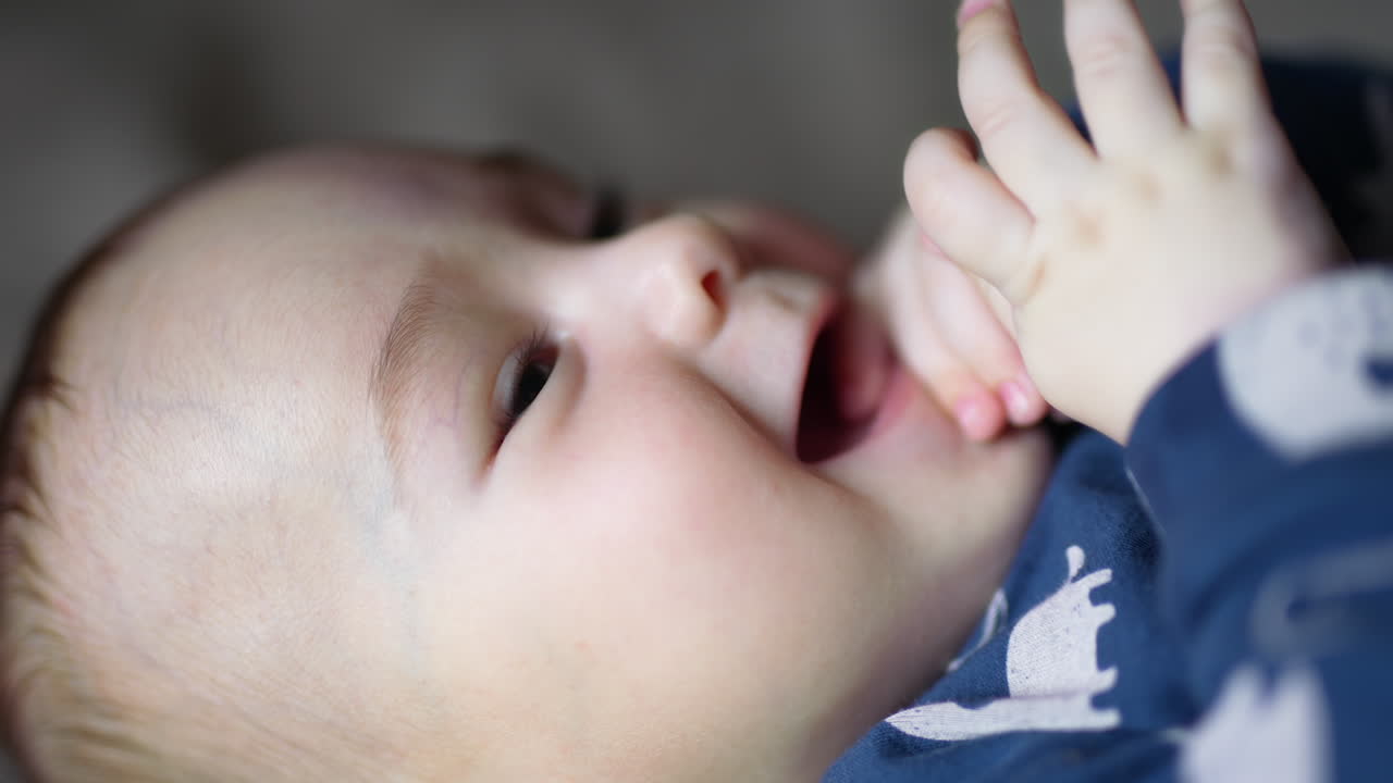 Head of a beautiful little child chewing his tiny finger. Smiley lovely kid in blue shirt close up. Side view.