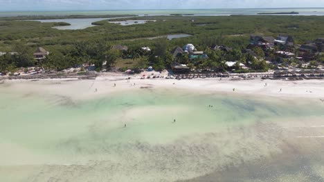 disparo de dron de gran angular que se desplaza hacia arriba de las concurridas playas de arena blanca frente a la costa de la isla tropical de holbox en méxico, filmado en 4k