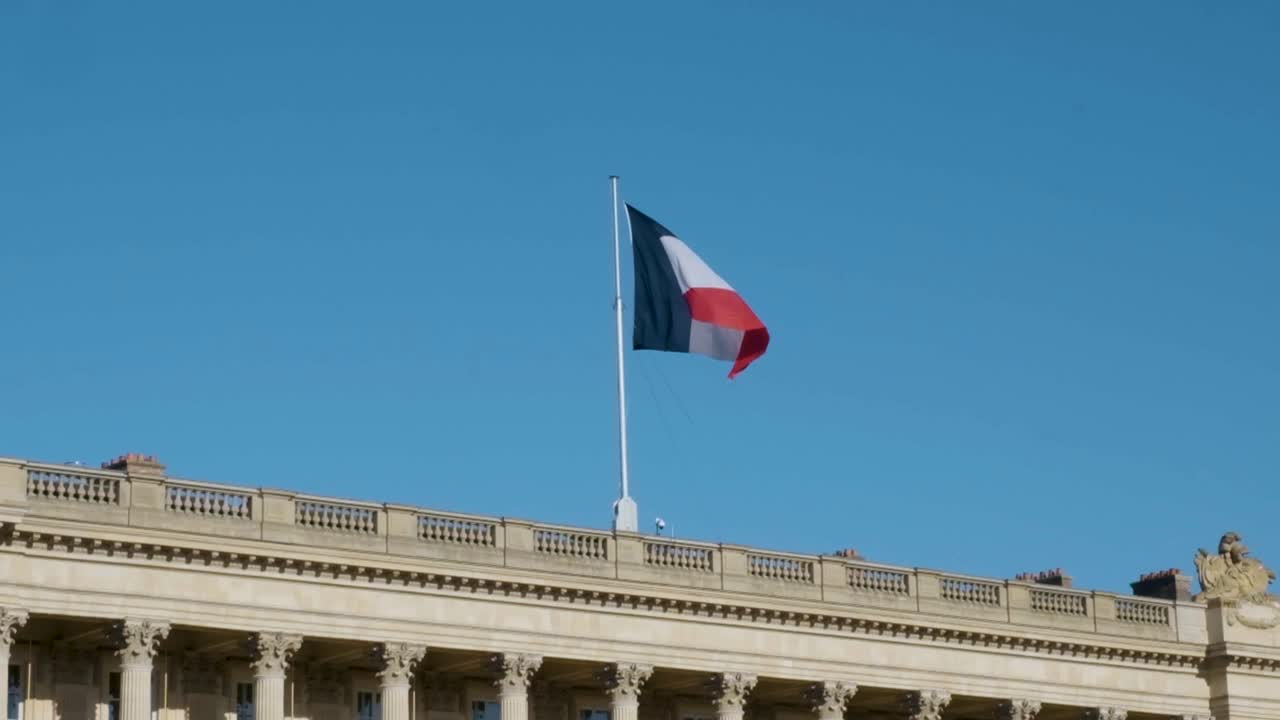 The wind animates the French flag against a bright blue Parisian sky, filmed in slow motion