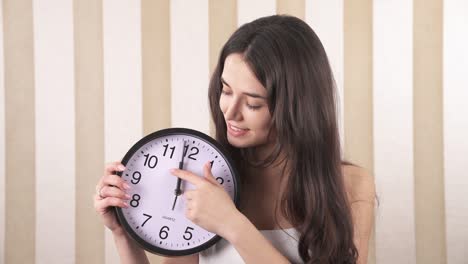 a close-up of a smiling girl. the girl is holding a wall clock in her hands and in one motion she moves the clock 2 hours ahead to the noon (midnight).