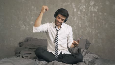 portrait of relax middle east businessman, ceo with headphones dancing on bed, listen to music in bedroom with mobile smartphone. entertainment leisure fun. people lifestyle at home.