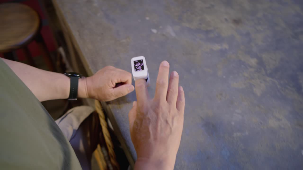 Senior Asian man clipping finger oximeter and adjusting at counter, monitoring readings, copy space