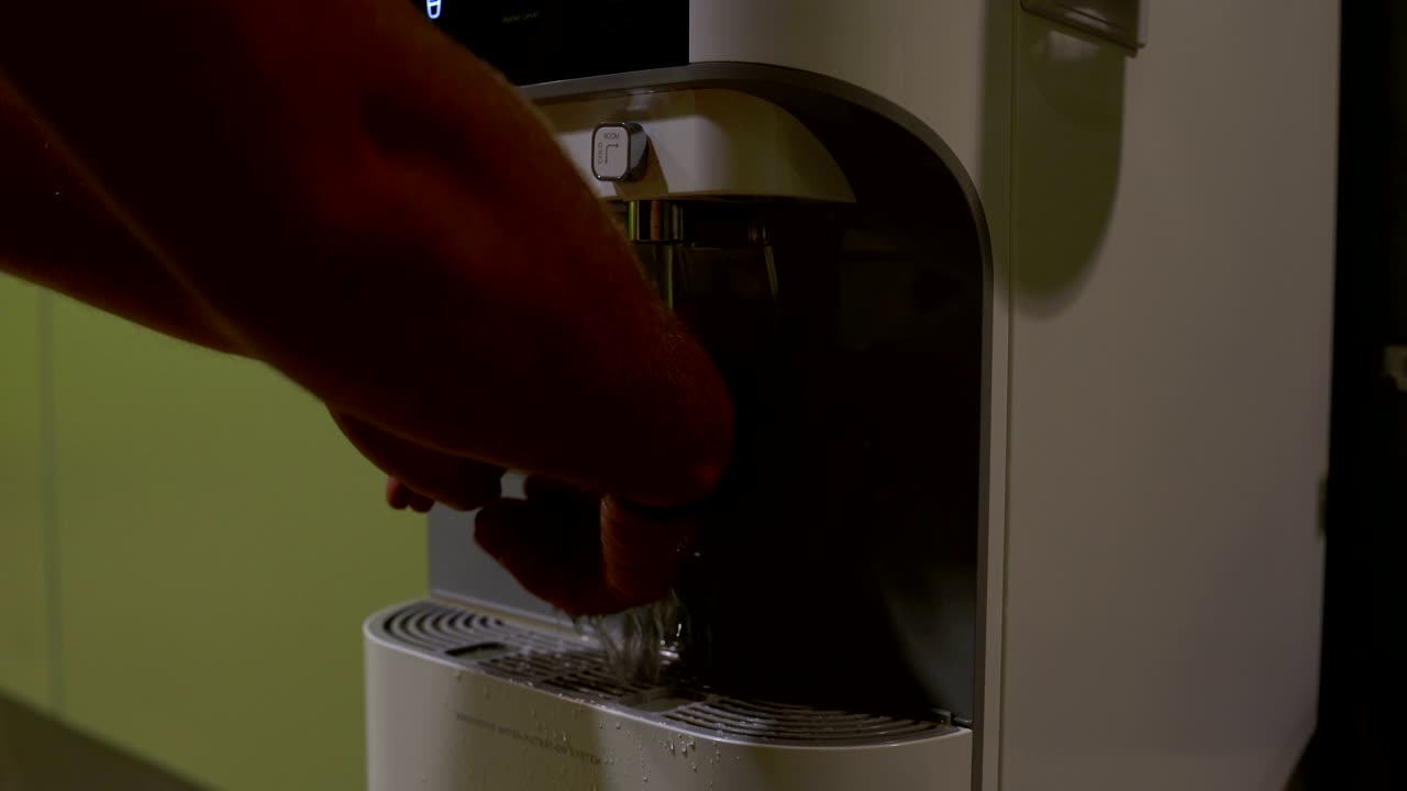 The man presses the button on the cooler and washes his hand with the clock
