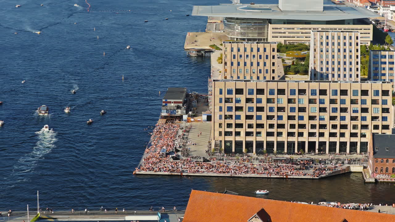 Aerial drone view of the busy Islands Brygge waterfront filled with swimmers, sunbathers, and cyclists in Copenhagen, Denmark