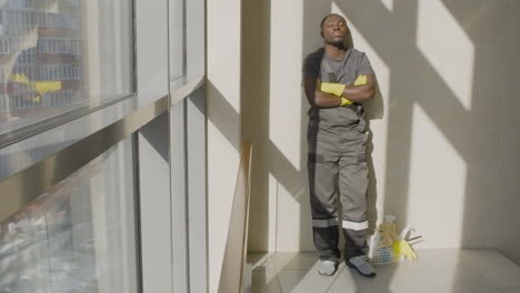 cleaning man with closed eyes resting and leaning on the wall while the sun shines through the window inside an office building