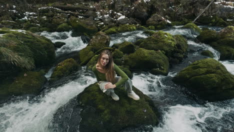 woman sitting on a rock by a mossy winter stream