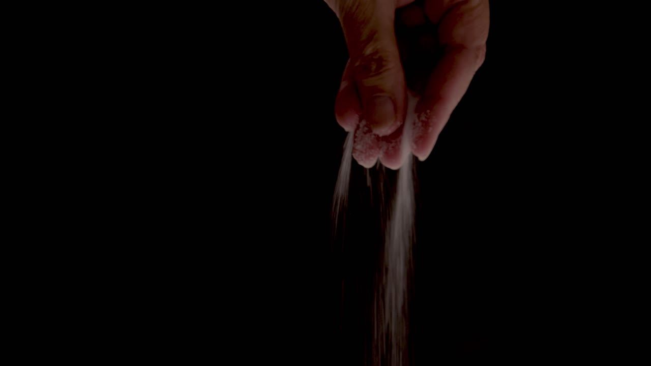 Salt being sprinkled onto food close up on a black backdrop