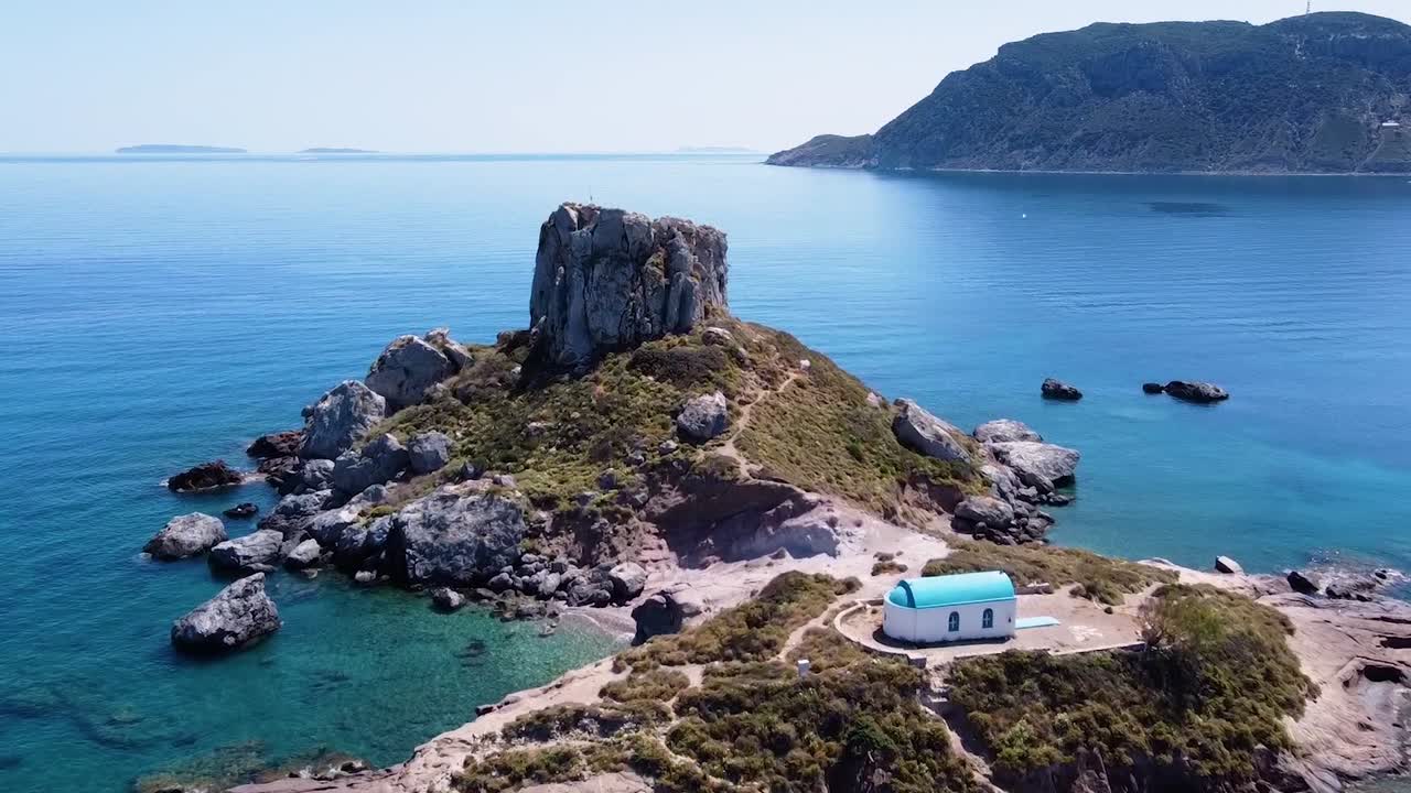 Cinematic drone shot of paradisiacal greek island with a small church on it.