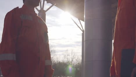 vista de cerca de dos trabajadores de la construcción en uniforme naranja y cascos estrechando la mano en el objeto de construcción