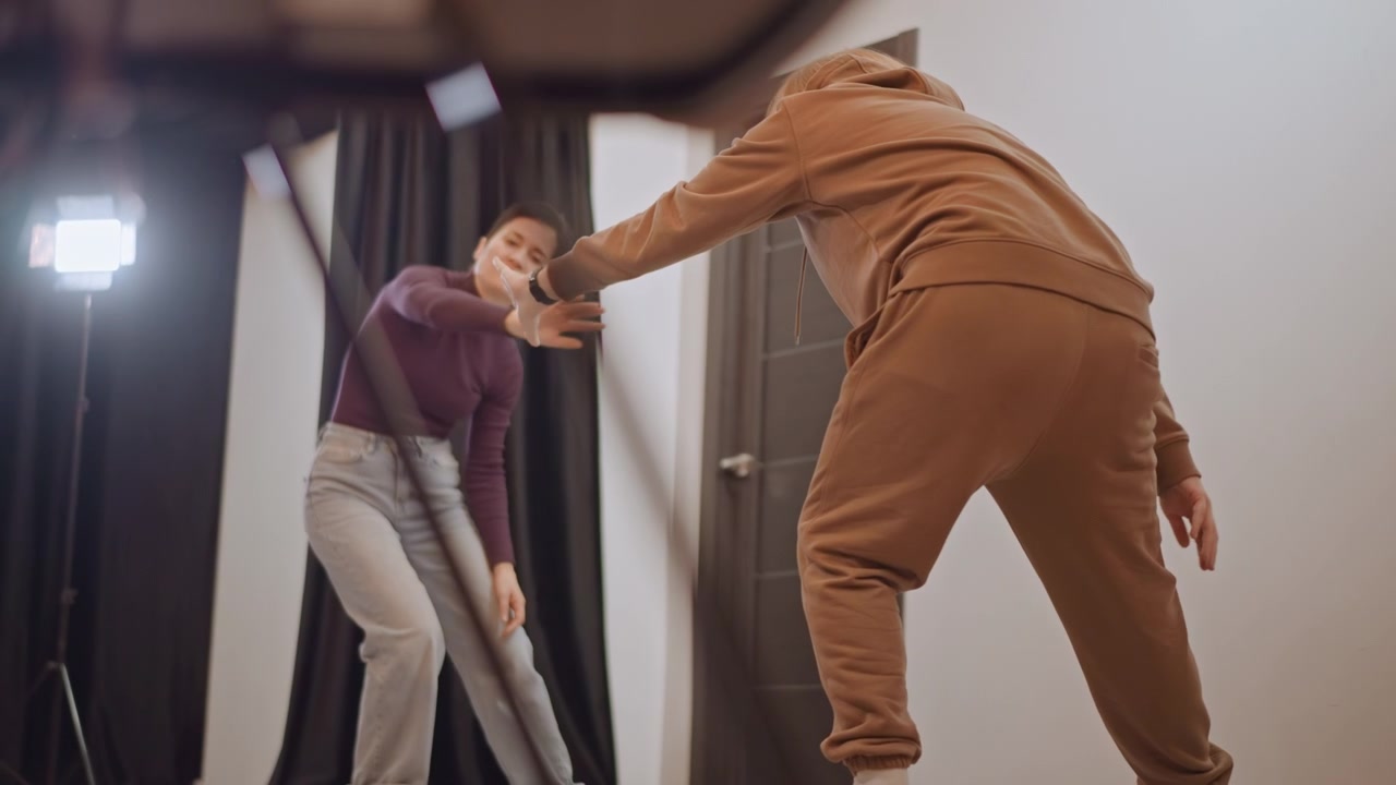 Intimate studio rehearsal with coach and student showing handson guidance and expressive warmup. Senior coach in brown tracksuit assists young performer through reach and posture adjustments, focused