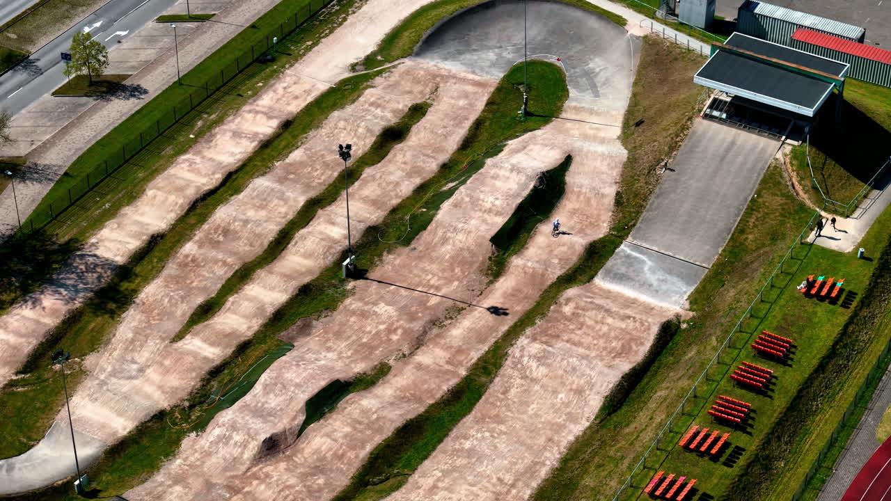 BMX rider circles pump track in city park loop, aerial overview orbit with curved layout