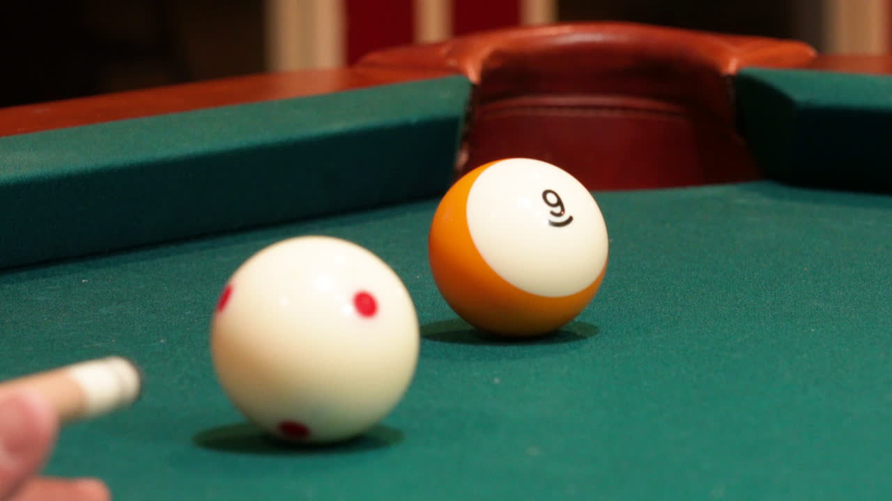 Closeup of Yellow Striped Nine Ball Being Shot Slow and Softly into the Corner Pocket of a Brunswick Pool Table after Practice Strokes using Cue Ball with Red Spots, Wooden Cue Stick and Green Felt