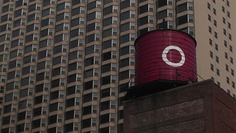 una antigua torre de agua con una gran o"" está en el primer plano de una toma de un edificio de apartamentos de gran altura""