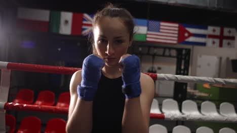 close up shot of confident female fighter with wrapped hands looking at camera while posing in gym