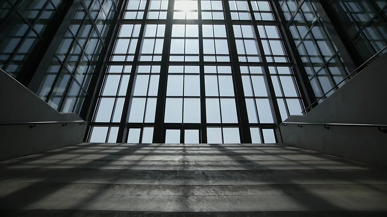 Luz solar cambiante proyectando sombras en forma de cuadrícula sobre escalones de hormigón hacia una ventana enrejada con barandillas de metal.