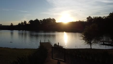 Wunderschöne-Aufnahme-Mit-Einer-Drohne-Bei-Sonnenuntergang-Auf-Einem-See-Mit-Wasserspiegel.-Die-Drohne-Bewegt-Sich-In-Einem-Gemälderahmen-Dem-Sonnenuntergang-Entgegen