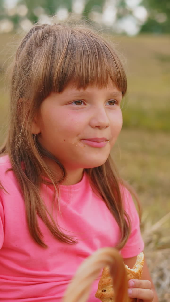 la niña disfruta de sus bocadillos al aire libre con una vista parcial de un niño sentado cerca, ambos disfrutando de pasteles en un campo abierto sereno rodeado de naturaleza y paisaje pacífico