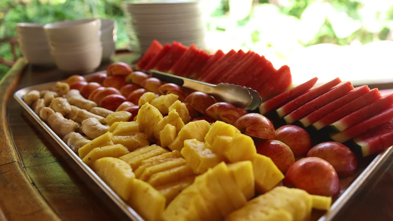 Healthy breakfast fruit snack tray on outdoor table with bowls and tongs