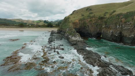 vista aérea de drones de las olas que se rompen en la costa escarpada y rocosa cubierta de algas y algas en la remota bahía de los caníbales, catlins, isla sur de nueva zelanda aotearoa