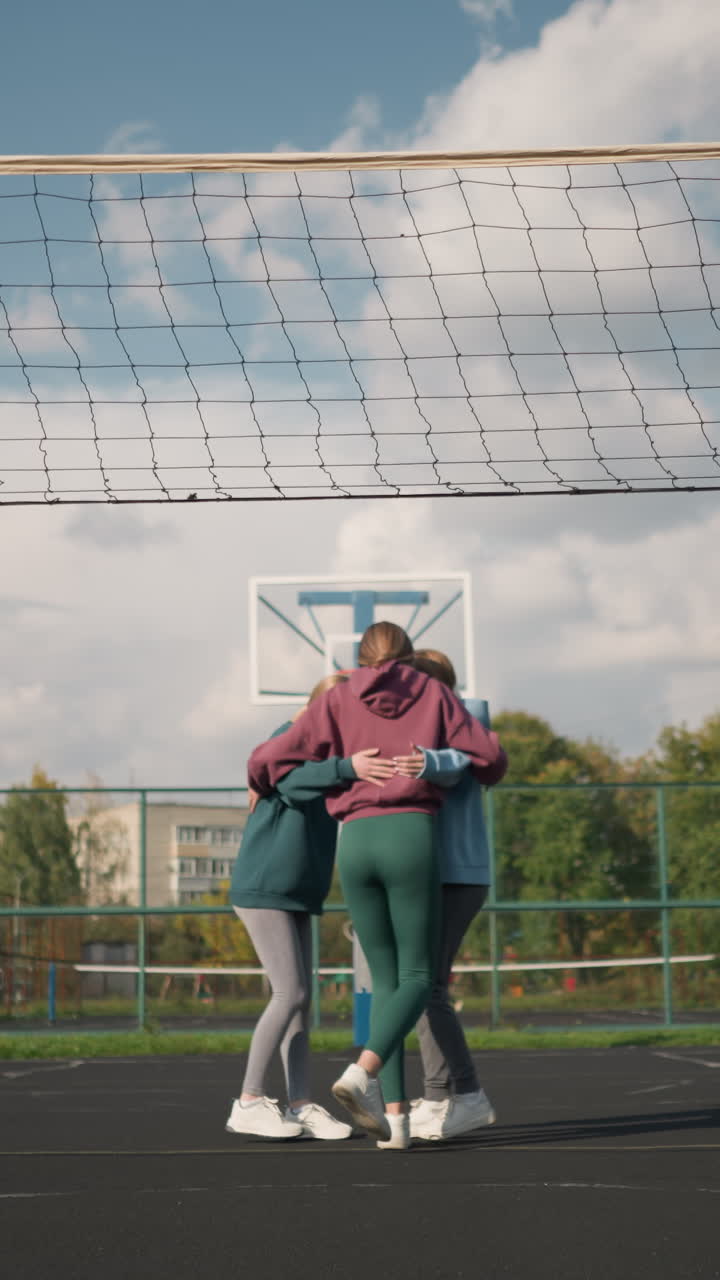 젊은이들이 푸른 야외 볼리볼 코트, 배경에 건물, 경기장에서 스포츠 시설, 밝은 낮에 야외에서 팀 활동을 즐기는 활발한 사람들의 그룹에서 행복하게 함께합니다.