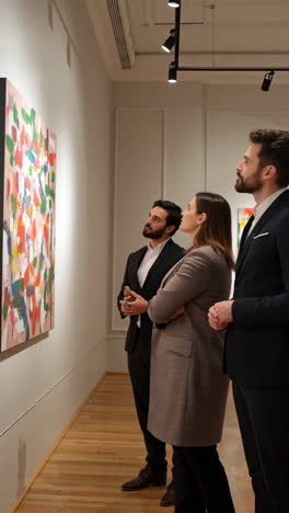 three people admiring an abstract painting in an art gallery