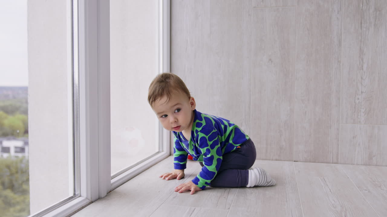 Lovely Caucasian baby looks curiously into window. Beautiful little boy moving by the floor in the room.