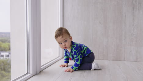 lovely caucasian baby looks curiously into window. beautiful little boy moving by the floor in the room.