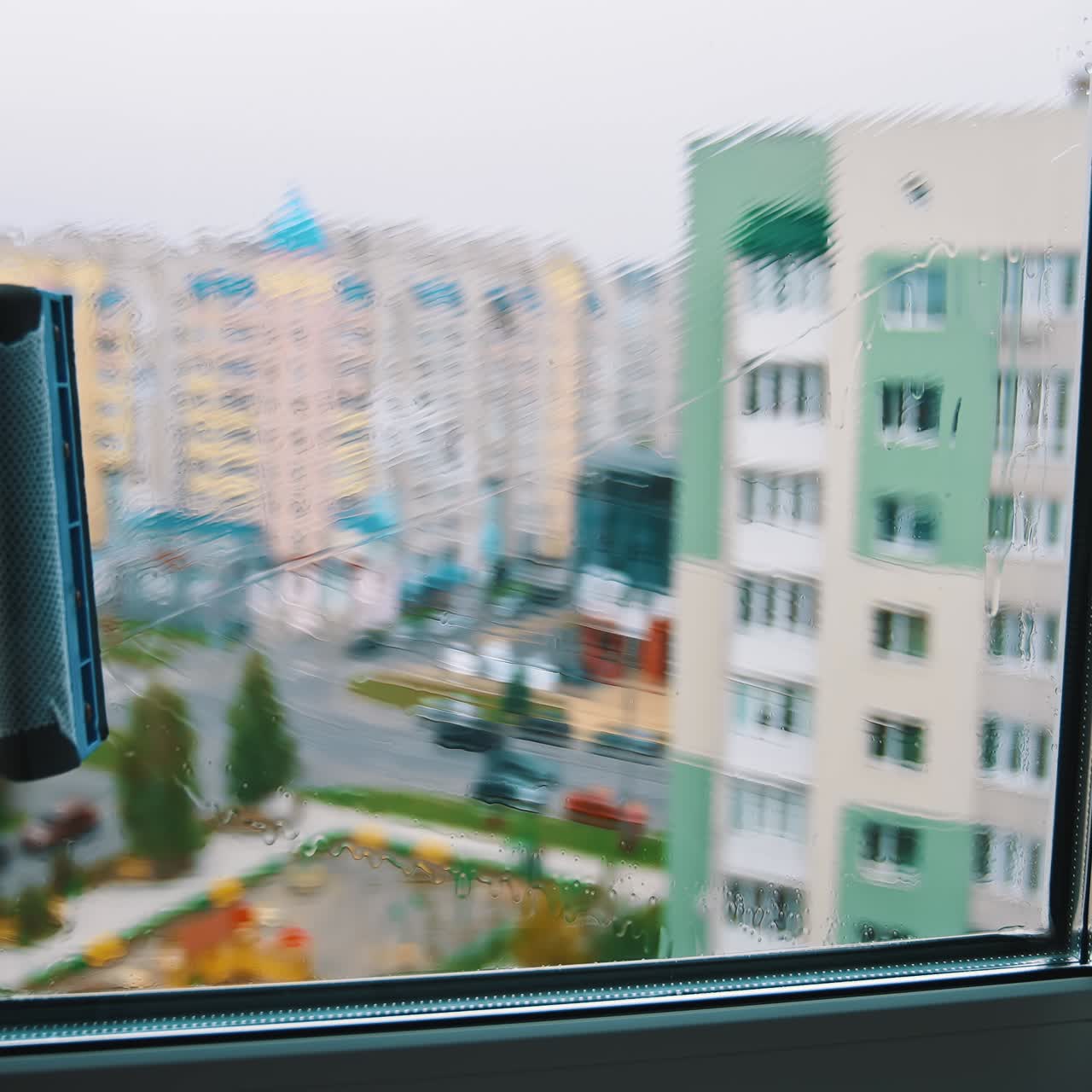 Brush washing window upstairs of a tall city building. Cleaning plastic window from outside on the urban background. View from indoors