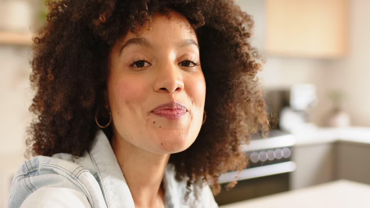 Woman sitting at kitchen counter with potted plant behind speaking to camera sharing message