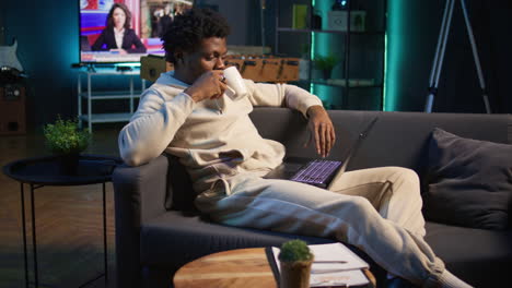 smiling male freelancer browsing the web on laptop in a modern apartment, demonstrating a lifestyle of independence. productivity in a virtual workspace, man multitasking. camera b.