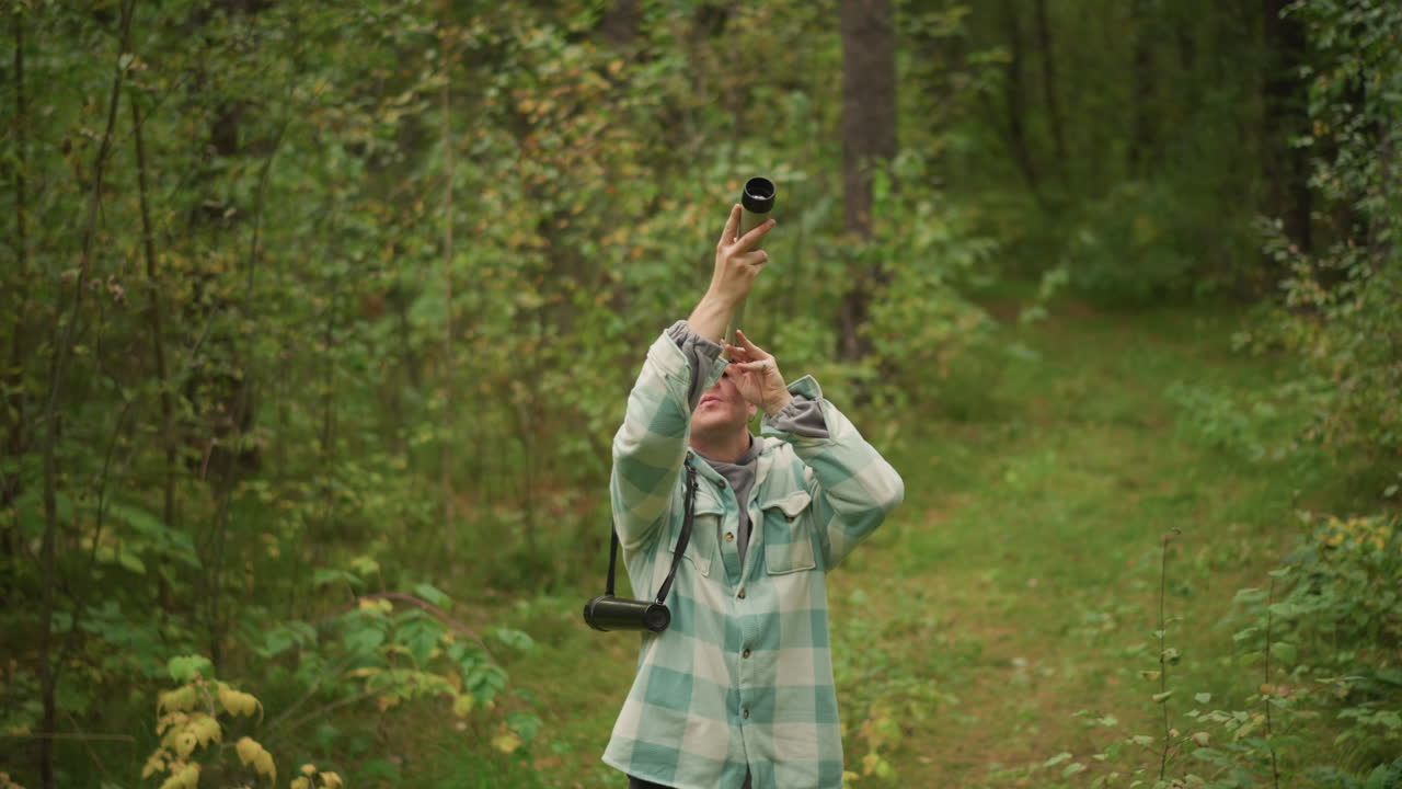 caucasian woodsman signaling with handmade horn on forest path, blowing rustic wooden horn, echoing sound across canopy, plaid jacket and beanie, backpack at side, nostalgic rural mood, solitude