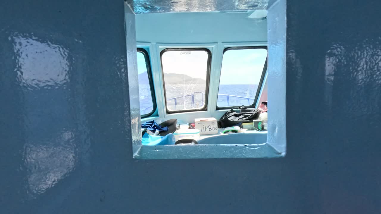 Camera moves backward through cabin window, revealing cluttered boat interior and bright daylight outside