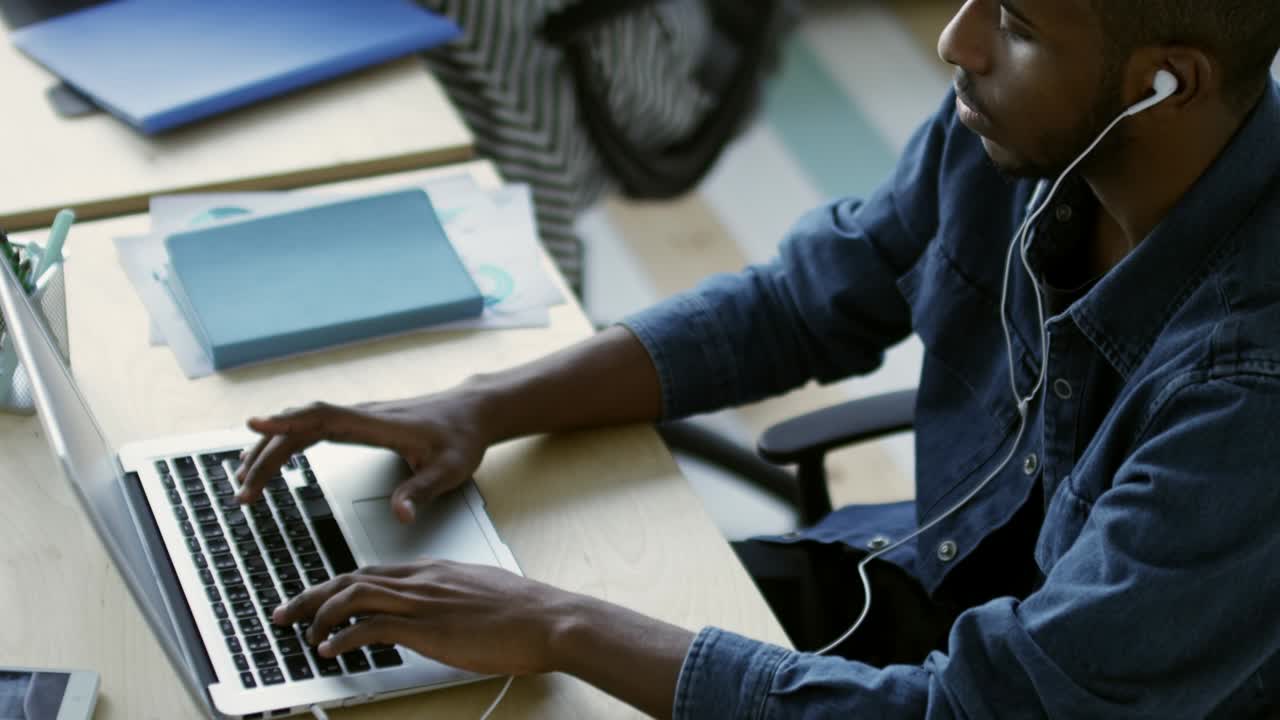 African Office Worker in Headphones Using Laptop