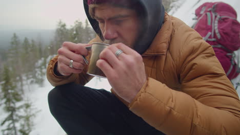 man drinking hot tea while camping in mountains