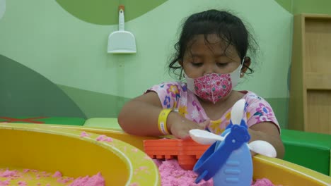 Cute-Asian-girl-playing-in-the-sandbox-on-the-playground-in-the-mall-during-covid-19-pandemic