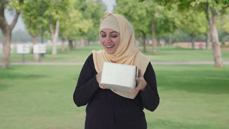 happy muslim woman receiving a gift in park