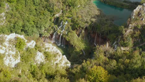 岩の多い崖と鬱蒼とした森の間の滝につながる明るいターコイズ ブルーの湖の信じられないほどの空撮ドローン ビュー